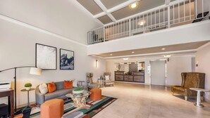 A spacious living area with a sofa, ottoman, and coffee table, a staircase to an upper level, and a kitchen in the background. - Best Western Plus Grand Manor Inn (Springfield)