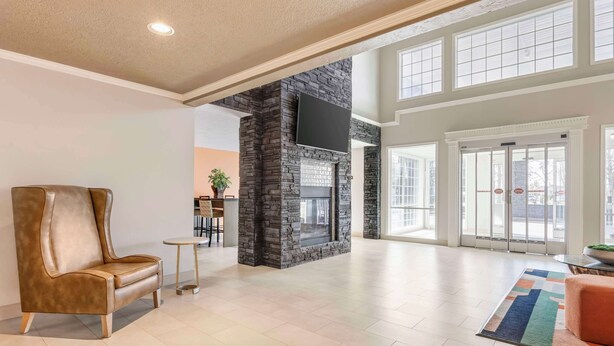 A spacious lobby with a stone fireplace, a comfortable leather sofa, and a large window providing natural light. - Best Western Plus Grand Manor Inn (Springfield)