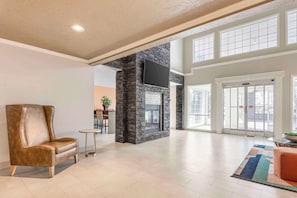 A spacious lobby with a stone fireplace, a comfortable leather sofa, and a large window providing natural light. - Best Western Plus Grand Manor Inn (Springfield)