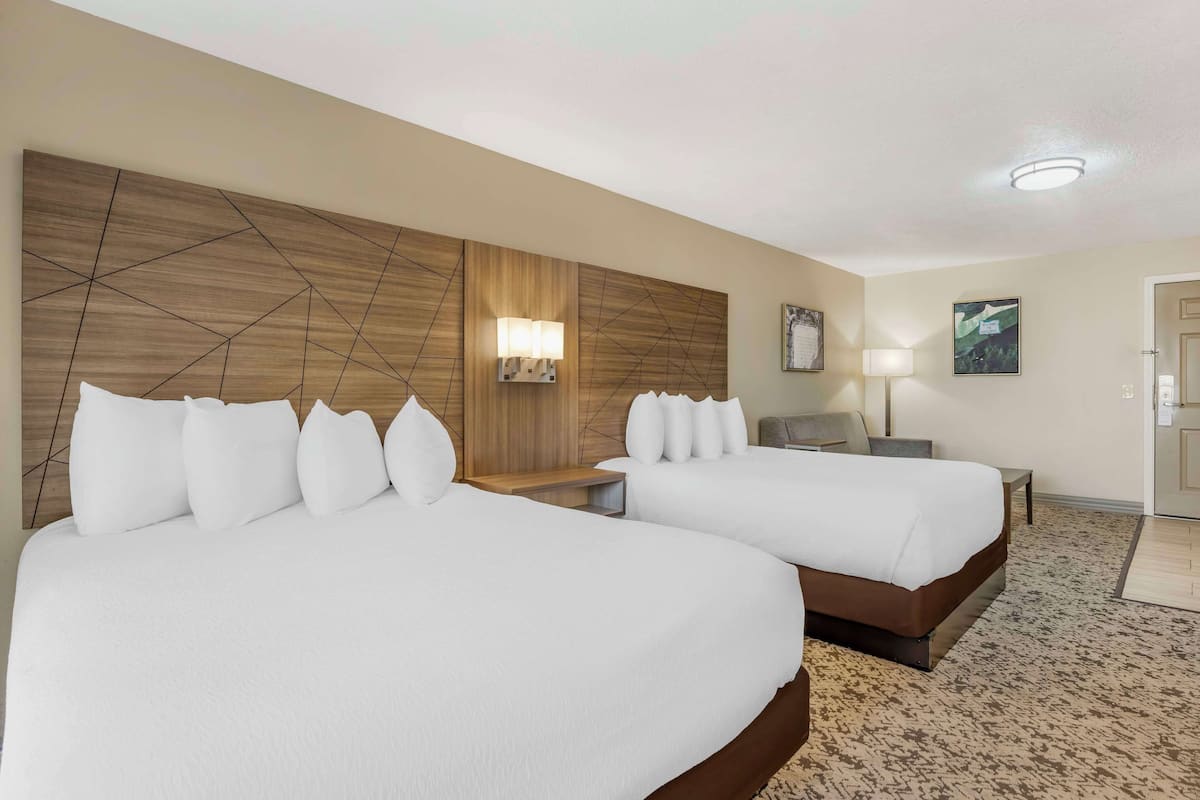 A hotel room with two beds, a wooden headboard, a nightstand, a lamp, and a framed picture on the wall.