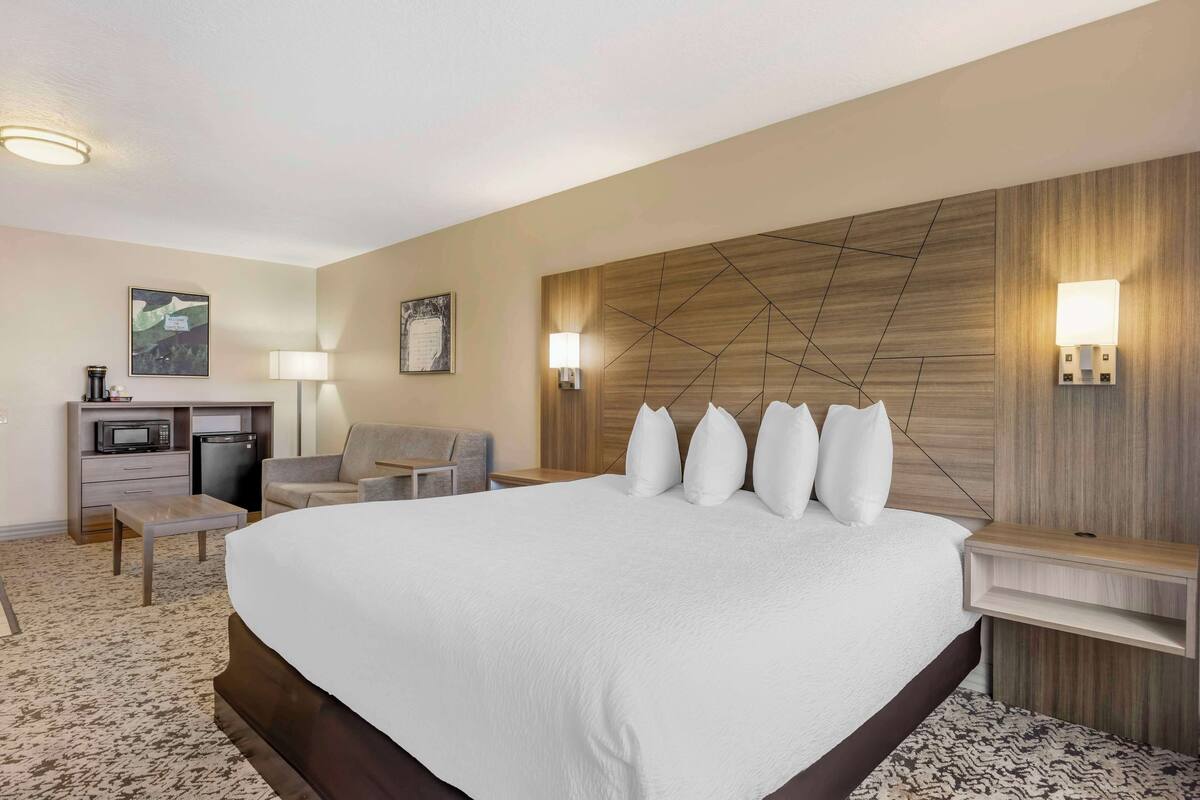 A hotel room with a large bed, a desk with a microwave, a chair, and two wall-mounted lamps.