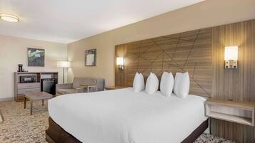 Habitación de hotel con una cama grande, un escritorio con microondas, una silla y dos lámparas de pared.