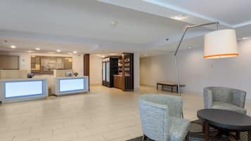 A hotel lobby with a reception desk, seating area, and a refrigerator stocked with beverages.