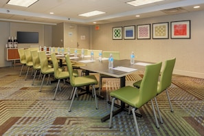 A conference room with a long table, multiple chairs, water bottles, a projector screen, and framed artwork on the wall. - Holiday Inn Express Milwaukee-West Medical Center by IHG (Milwaukee)