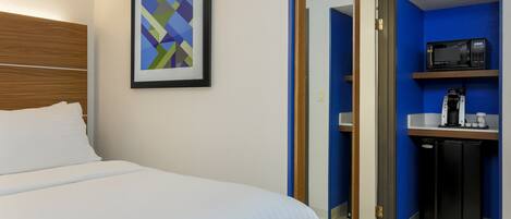 A hotel room with a bed, a framed abstract painting, a microwave, a coffee maker, and a refrigerator.