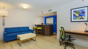 A modern living room with a blue sofa, a wooden coffee table, and a desk with a chair. - Holiday Inn Express Milwaukee-West Medical Center by IHG (Milwaukee)