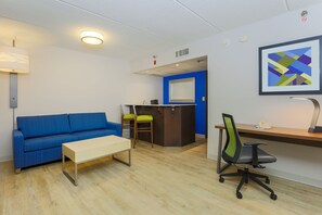 Uma sala de estar moderna com um sofá azul, uma mesa de centro de madeira e uma escrivaninha com uma cadeira.