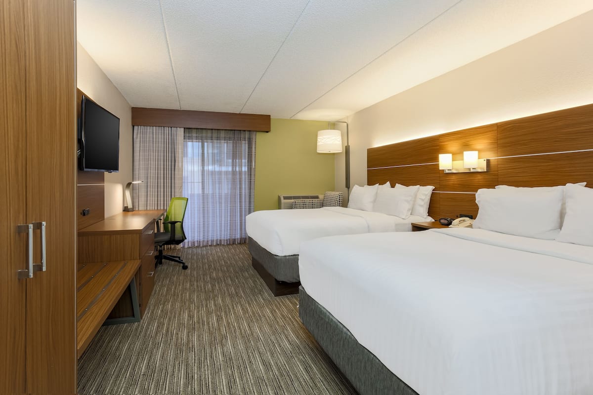 A hotel room with two beds, a desk with a chair, a television, and a window with curtains.