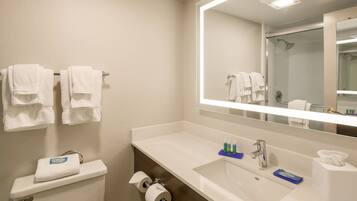A hotel bathroom with a white sink, a mirror, a toilet, and a towel rack with multiple towels.