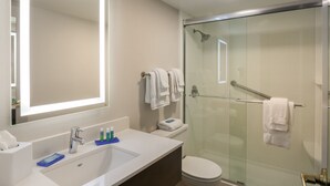 A modern bathroom with a glass-enclosed shower, a large mirror, and a white sink with toiletries. - Holiday Inn Express Milwaukee-West Medical Center by IHG (Milwaukee)