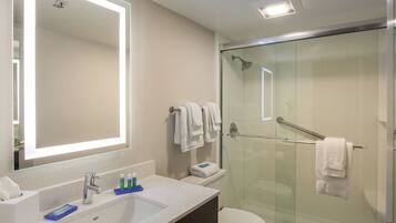 A modern bathroom with a glass-enclosed shower, a large mirror, and a white sink with toiletries.