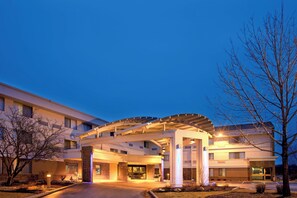 Entrada de un hotel con un vestíbulo cubierto, fachada de ladrillo y un árbol en primer plano.