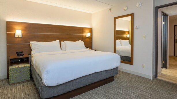 A hotel room with a large bed, a nightstand, a mirror, and a carpeted floor. - Holiday Inn Express Milwaukee-West Medical Center by IHG (Milwaukee)