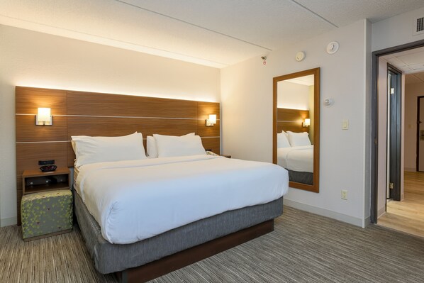 Quarto de hotel com uma cama grande, uma mesa de cabeceira, um espelho e piso coberto por carpete.
