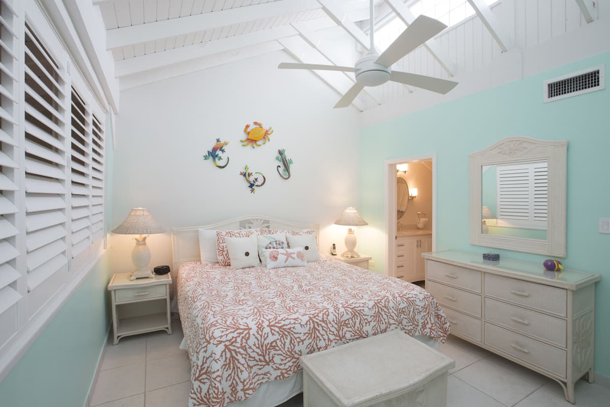 Quarto com cama, duas mesas de cabeceira com abajures, cômoda, espelho e ventilador de teto.