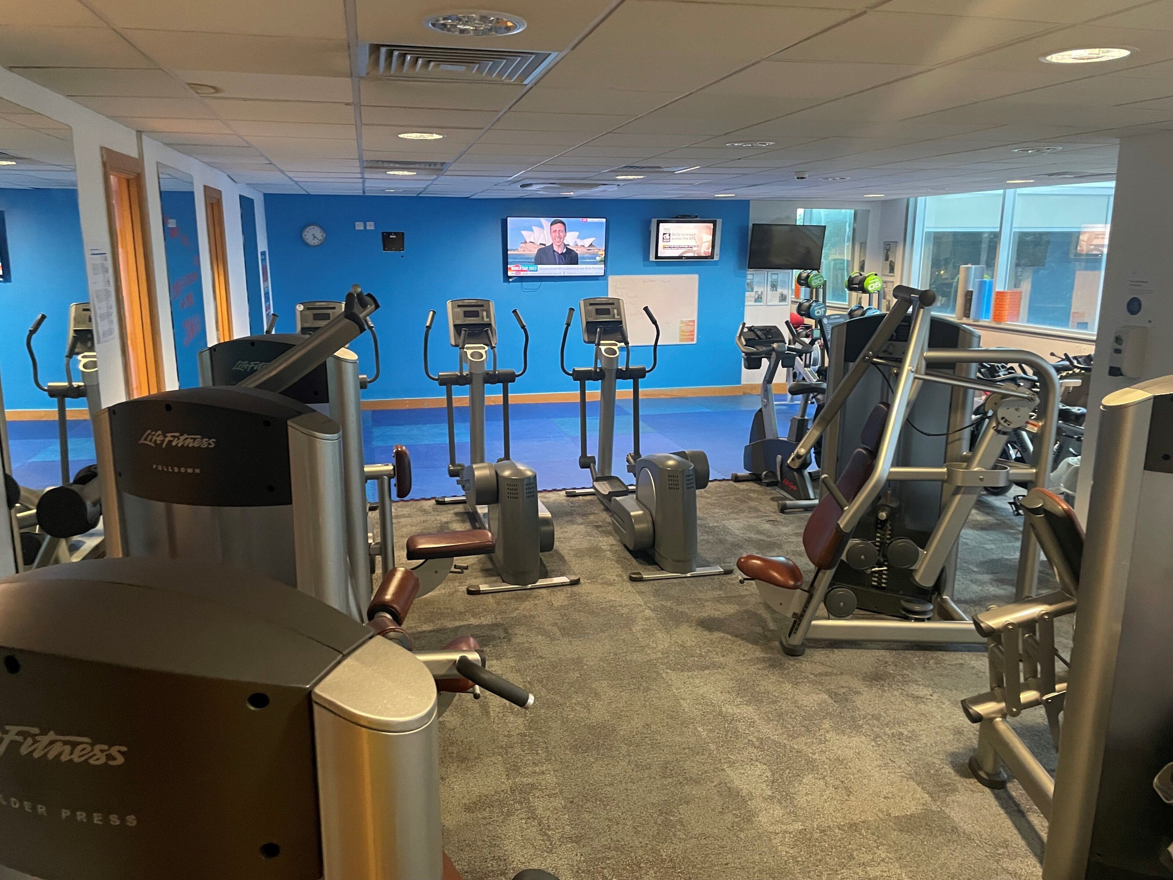 Un gimnasio con diverso equipo de ejercicio, una pantalla de televisión y una pared azul.