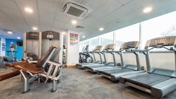 Un gimnasio con cintas de correr, máquinas de pesas y una pared azul con un reloj.