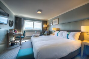 A hotel room with a large bed, a desk with a chair, a window with a view, and a flat-screen TV mounted on the wall. - Holiday Inn Edinburgh Zoo by IHG (Edinburgh)