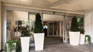 L’entrée d’un hôtel, avec une porte en verre, des plantes en pot et une enseigne bien visible indiquant « Holiday Inn ».