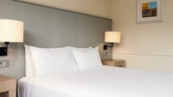 A neatly made bed with white linens in a hotel room, two bedside lamps, and a framed picture on the wall.