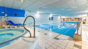 Une piscine intérieure avec un sol carrelé de bleu, un jacuzzi et des chaises longues bleues.