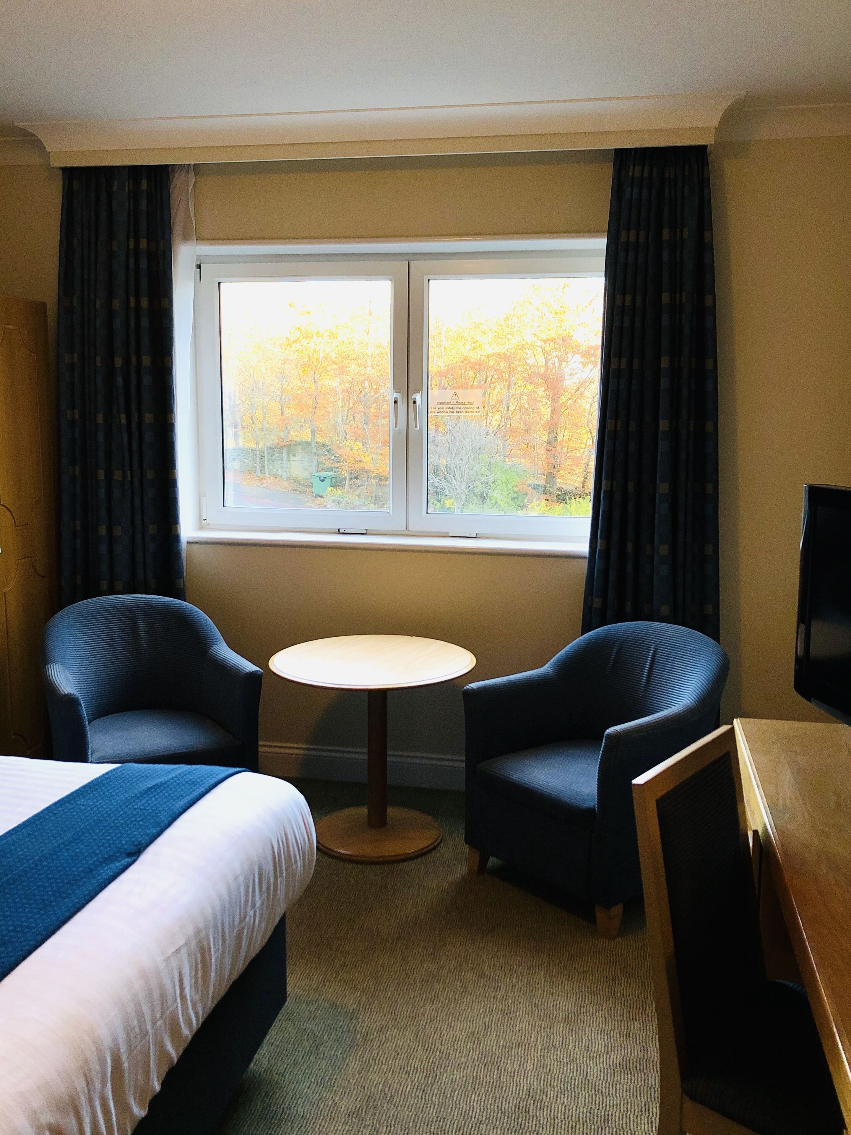 A hotel room with a bed, two armchairs, a small round table, and a window with curtains.