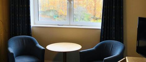 A hotel room with a bed, two armchairs, a small round table, and a window with curtains.