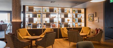 A lobby with a central seating area, a bookshelf with various items, and a fire extinguisher on the wall.