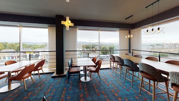 A modern dining area with large windows, a patterned carpet, and a variety of seating options.