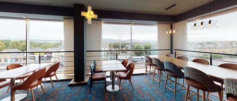 A modern dining area with large windows, a patterned carpet, and a variety of seating options.