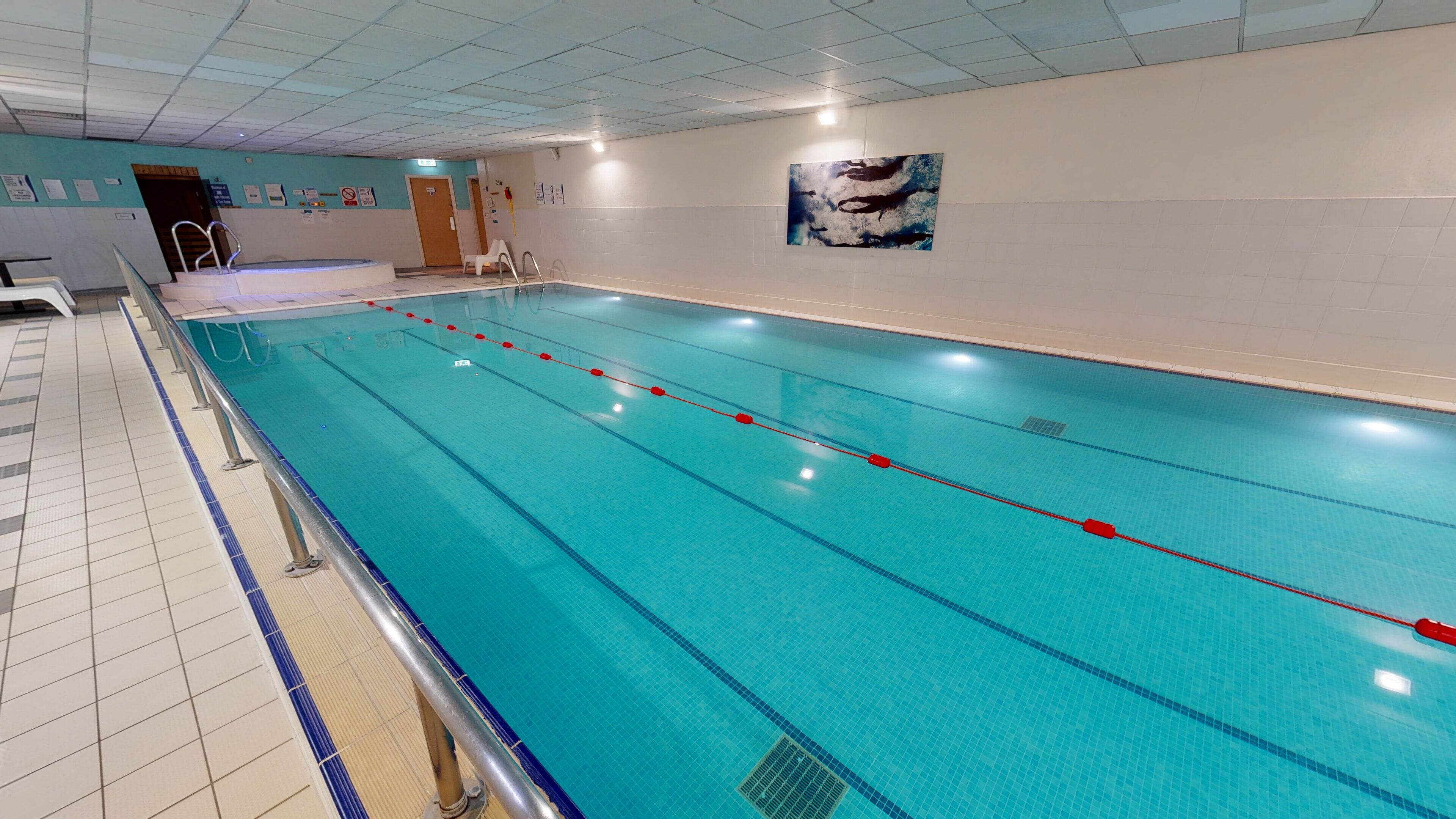 A long indoor swimming pool with clear lanes, a tiled floor, and a wall-mounted artwork.