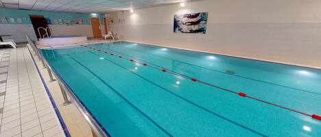 A long indoor swimming pool with clear lanes, a tiled floor, and a wall-mounted artwork.