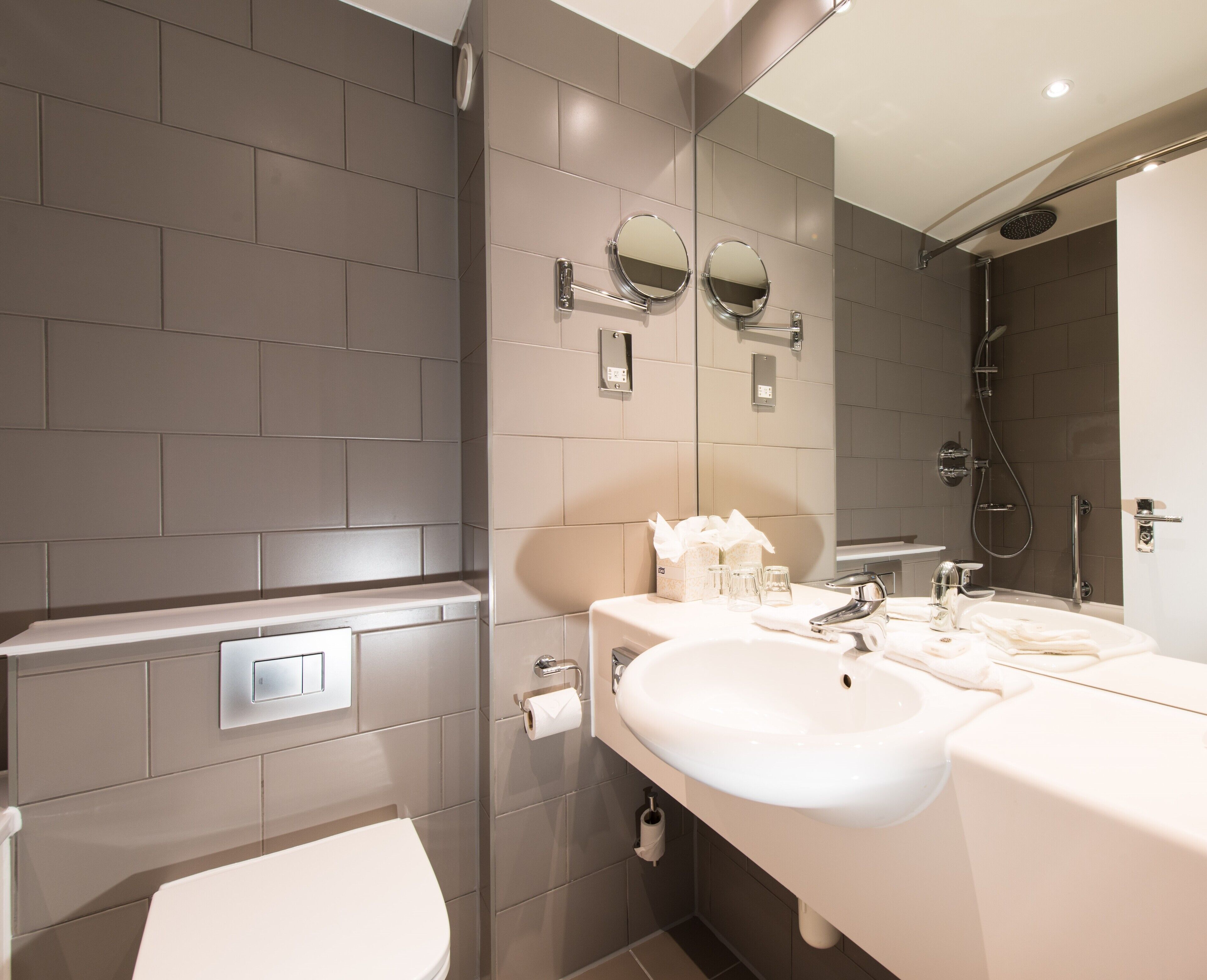 A modern bathroom with a toilet, two sinks, a shower, and a mirror.