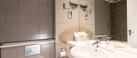 A modern bathroom with a toilet, two sinks, a shower, and a mirror.