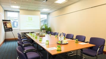 A conference room with a long table, chairs, a projector screen, and a presentation about Holiday Inn Edinburgh.