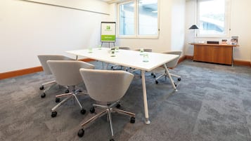 Un salón de conferencias con una mesa blanca, sillas grises, una rotafolio y un escritorio con un menú.
