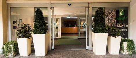A Holiday Inn entrance with glass doors, a reception desk, and potted plants.