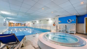 An indoor swimming pool with a hot tub, lounge chairs, and a lifebuoy on the wall.
