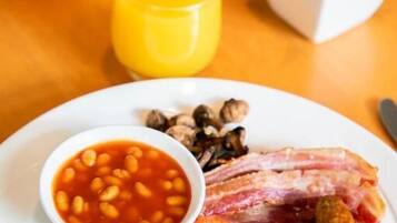 A breakfast plate with eggs, bacon, sausages, beans, toast, and a tomato.