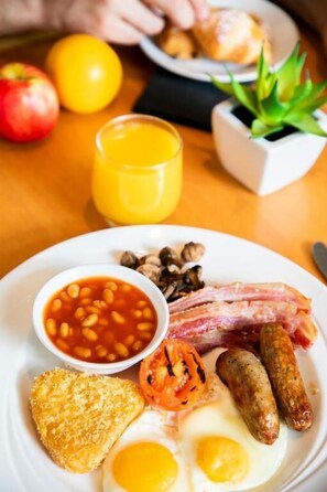 A breakfast plate with eggs, bacon, sausages, beans, toast, and a tomato.