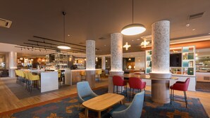 Un hall d’hôtel moderne avec un bar, des espaces aménagés pour s’asseoir et un tapis à motifs.