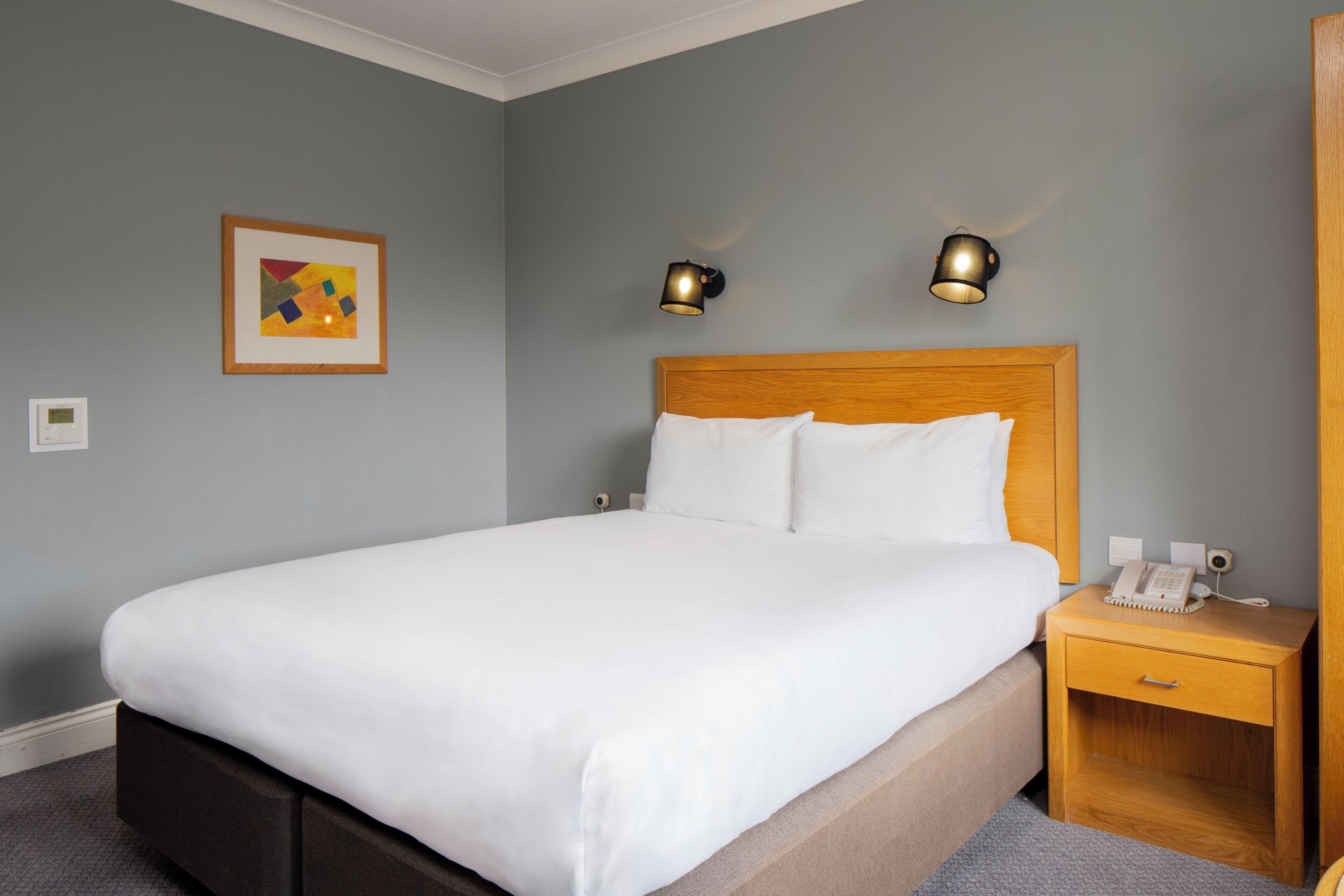 A neatly made bed with white linens, a wooden headboard, and two bedside lamps.