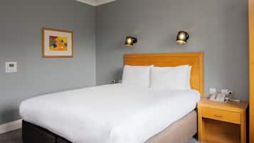 Una cama bien hecha con sábanas blancas, cabecera de madera y dos lámparas de noche.