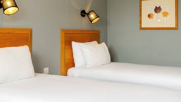 A hotel room with two beds, a framed artwork on the wall, and wall-mounted lamps.