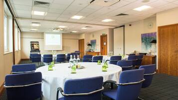 A conference room with a round table, blue chairs, and a projector screen.