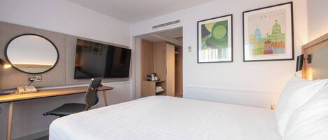 Une chambre d’hôtel avec un grand lit, un bureau avec une chaise, une télévision et deux tableaux encadrés au mur.