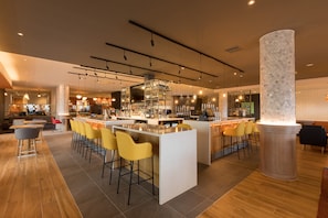 A modern bar area with a central island, bar stools, and a variety of bottles and glasses on shelves.