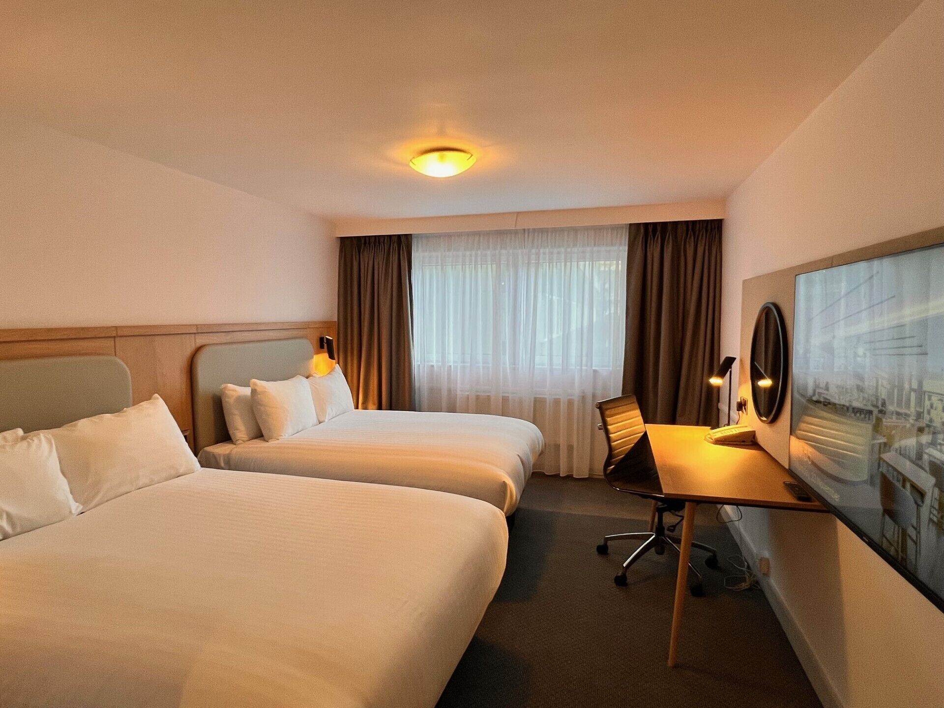 Una habitación de hotel con dos camas, un escritorio, una silla y un ventanal con cortinas.