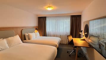 Una habitación de hotel con dos camas, un escritorio, una silla y un ventanal con cortinas.