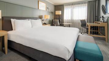 A hotel room with a large bed, a desk, a chair, a small table, and a bench.